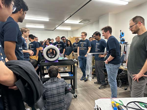 Hackathon participants seen gathered around partially built MRI scanner in NYU Langone's low-field laboratory.