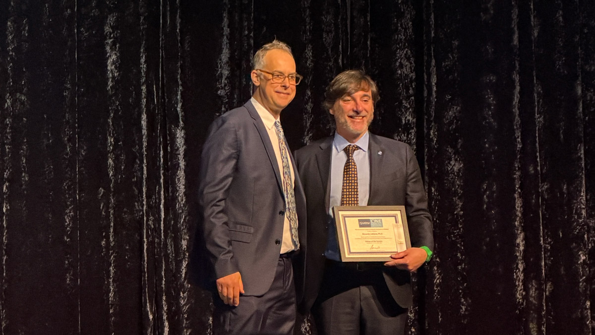 Photo: Mark Griswold posing on a stage next to Riccardo Lattanzi, who is holding a certificate.